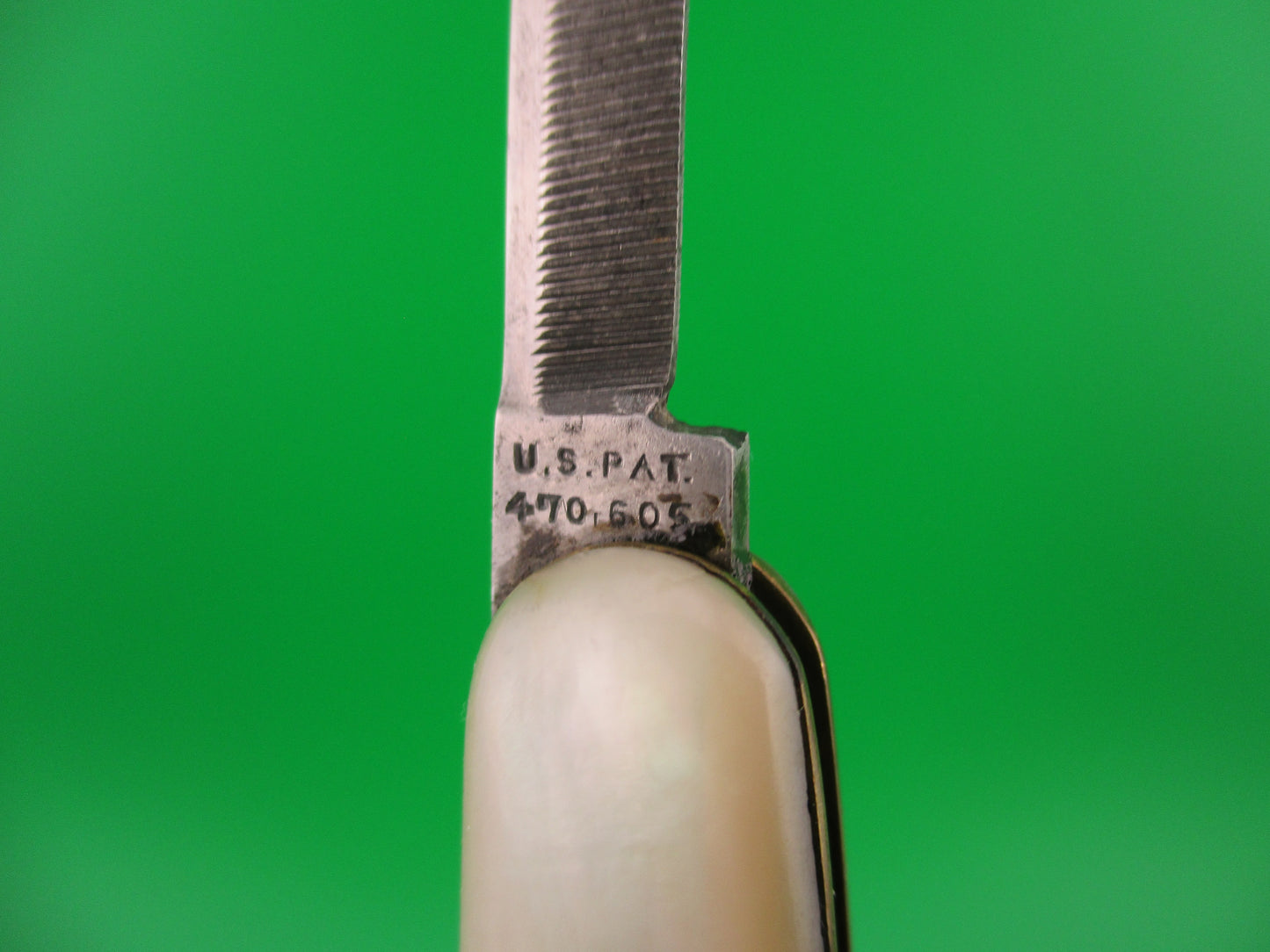 Close-up of a pocket knife blade with 'U.S. Pat' engraving on a green background