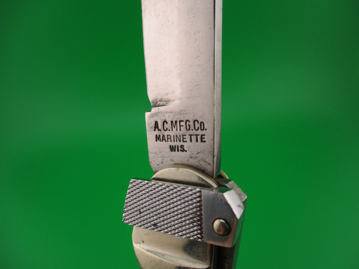 Close-up of a knife blade with 'A.C. MFG. CO. Marinette, WIS.' engraving on a green background