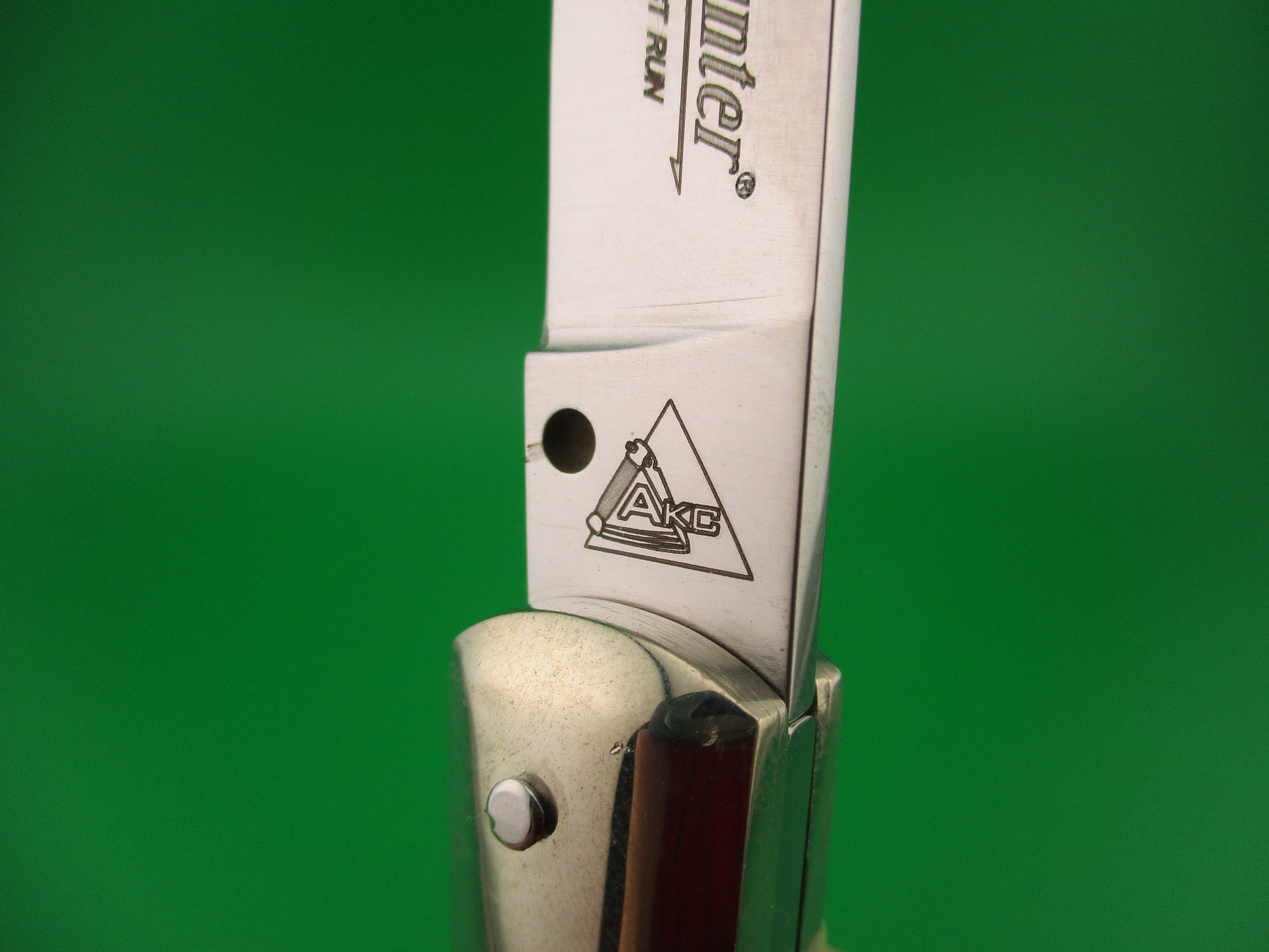 Close-up of a knife with a visible brand logo on a green background