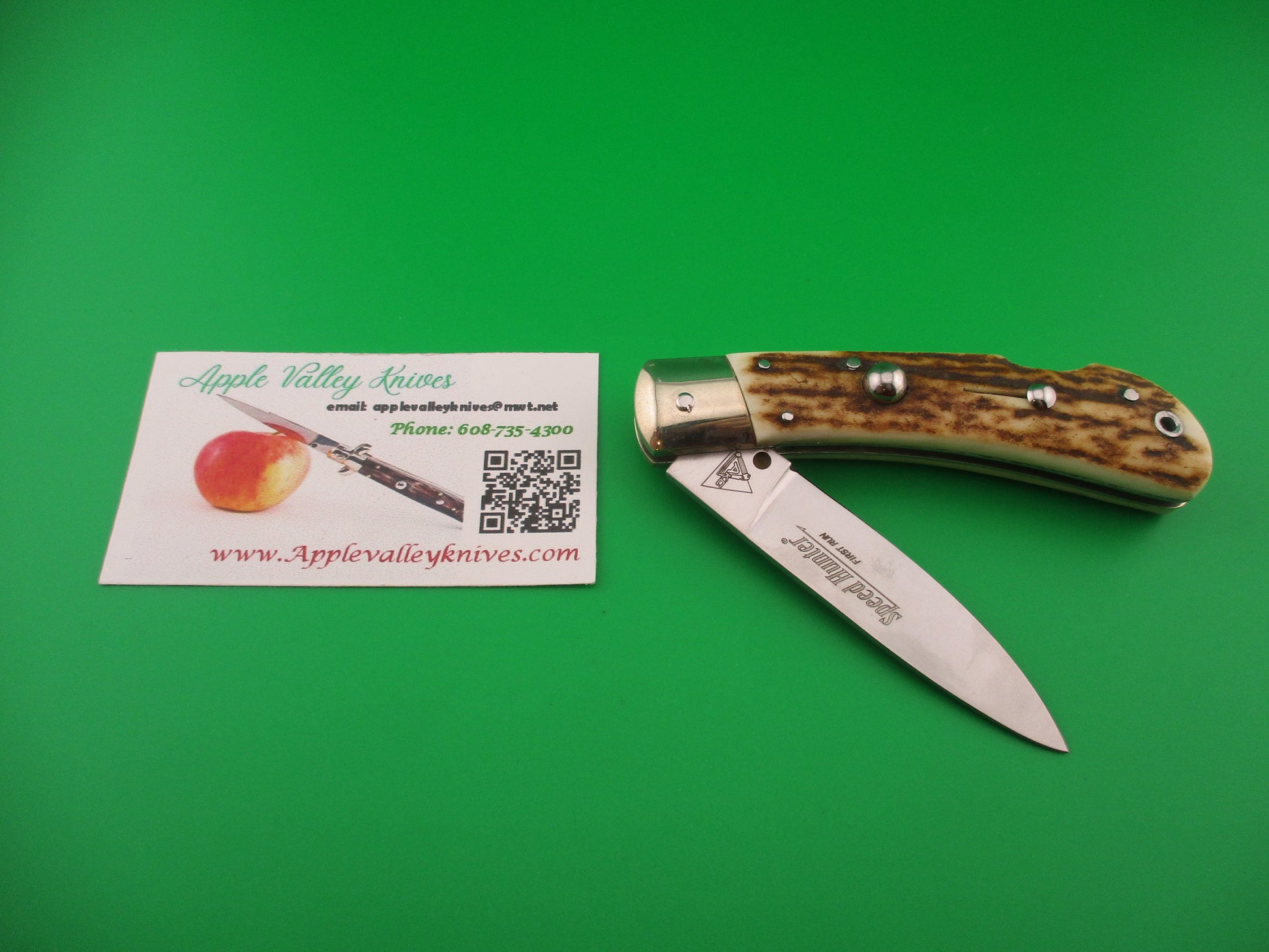 Pocket knife with staghorn handle next to an Apple Valley Knives business card on a green background