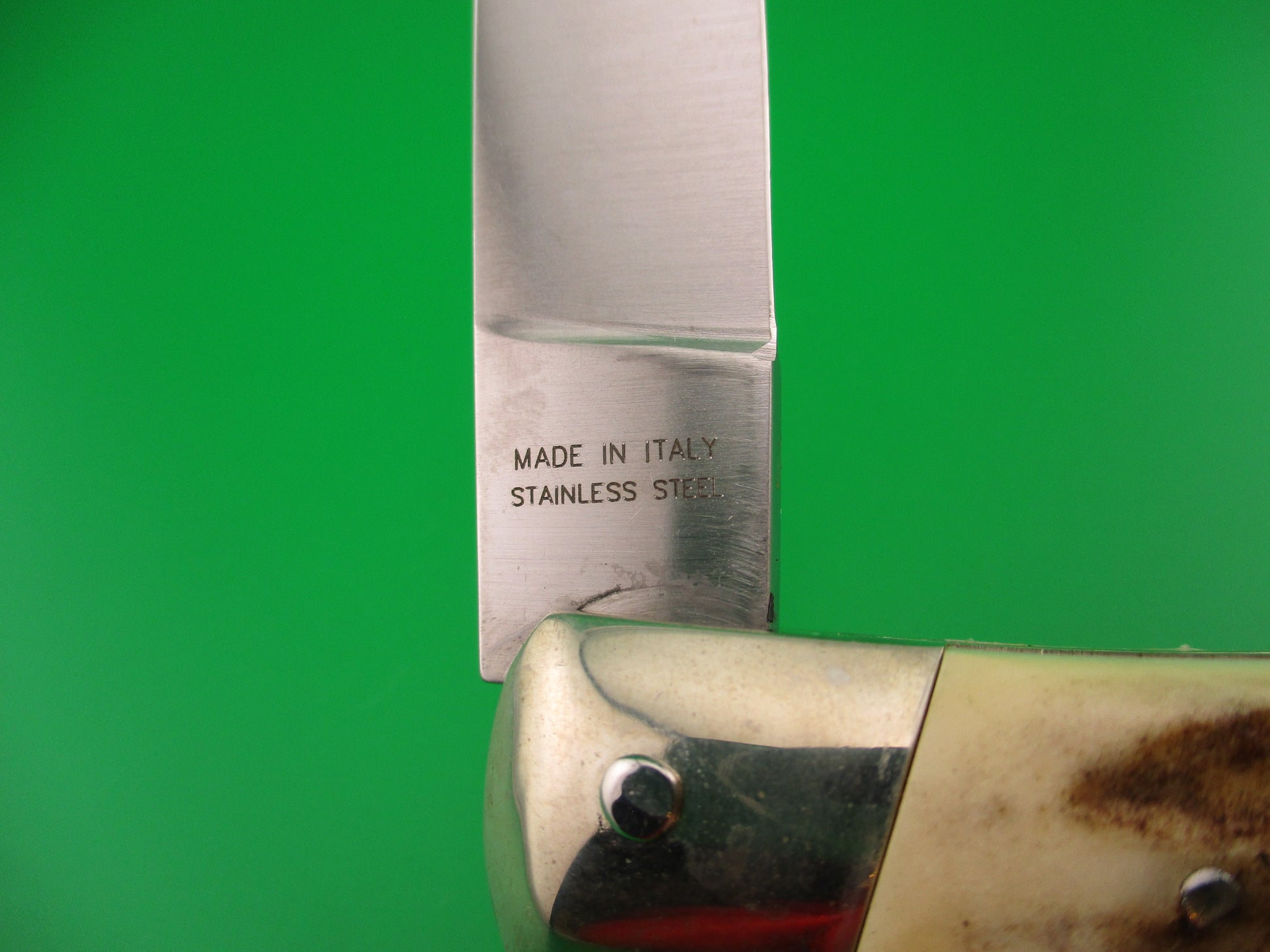 Knife blade with 'Made in Italy Stainless Steel' engraving on a green background