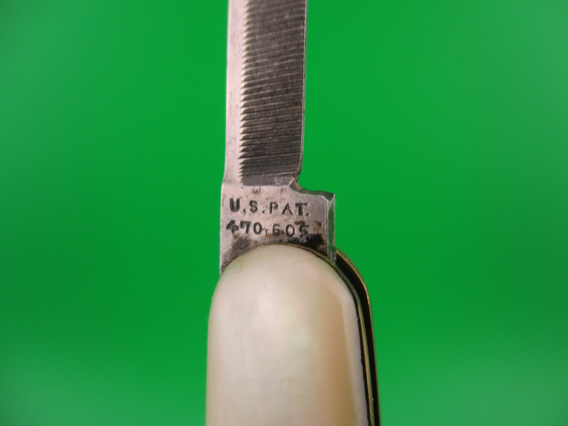 Close-up of a pocket knife blade with 'U.S. Pat' engraving on a green background