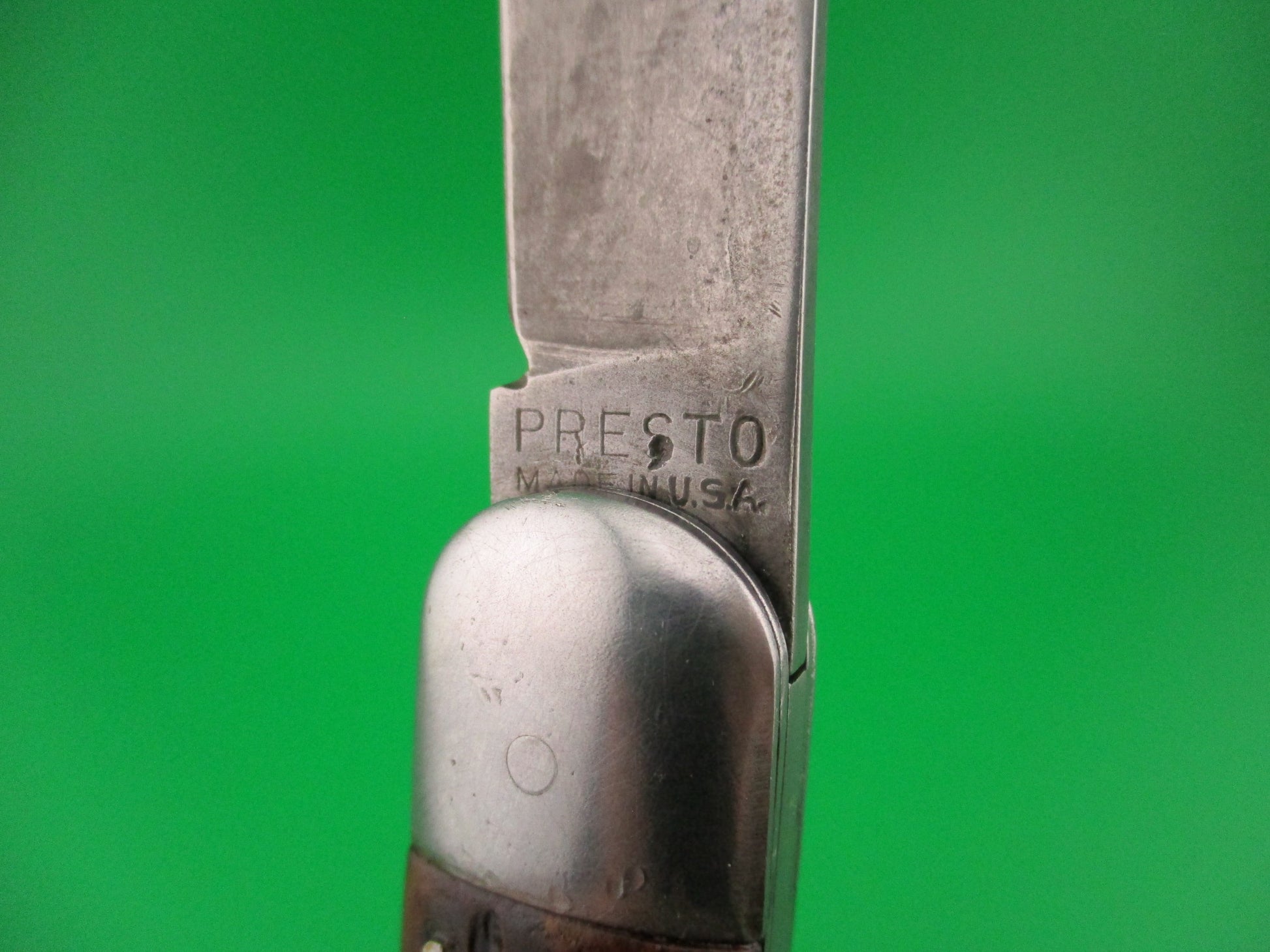 Close-up of a knife blade with 'Presto' branding on a green background