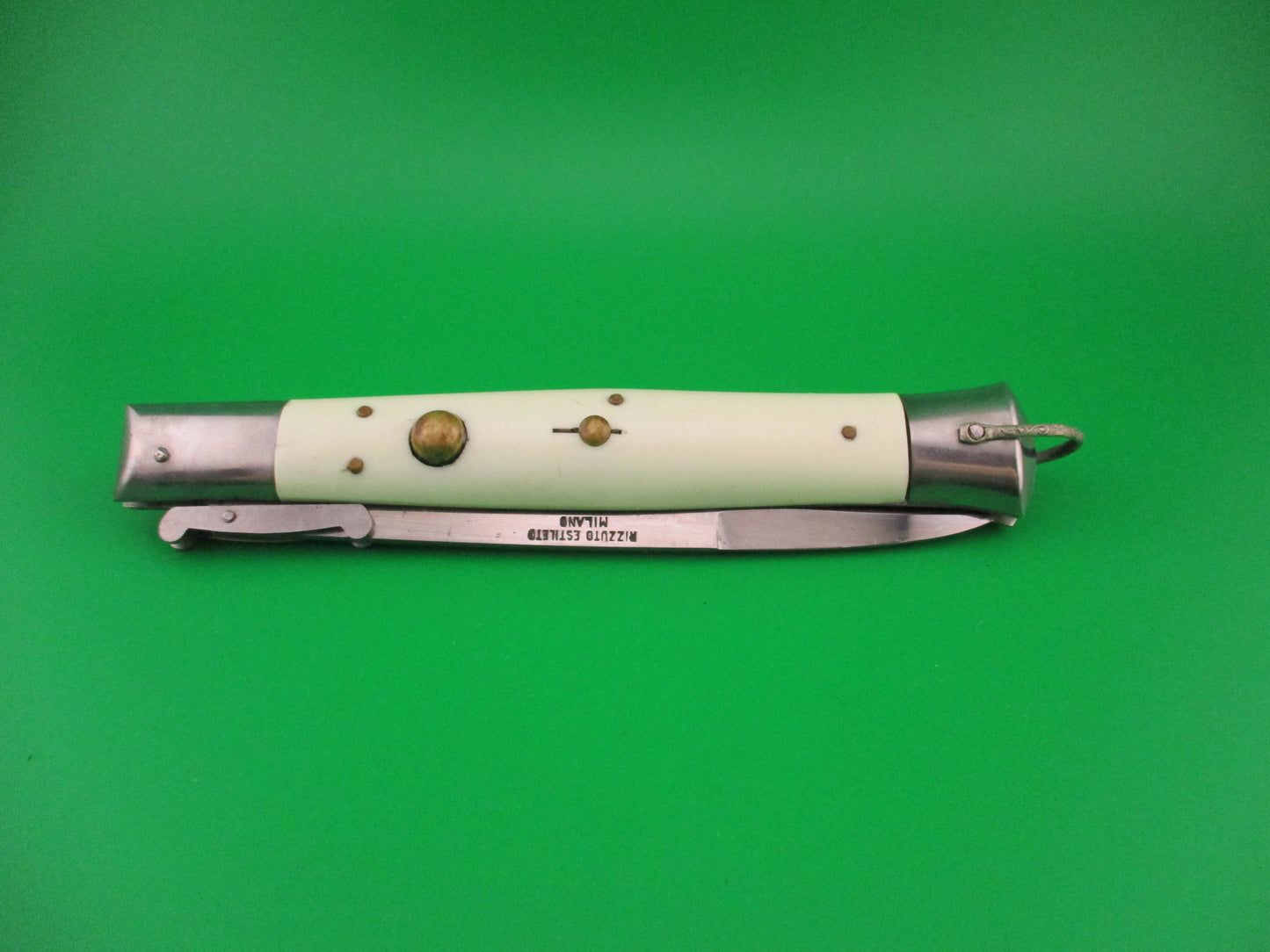 Foldable knife with a white handle and silver blade on a green background